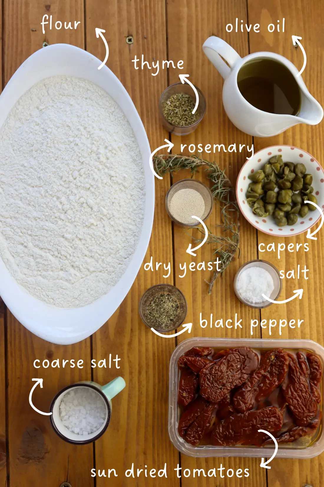 gathering ingredients for a focaccia with sun dried tomatoes: flour, sun dried tomatoes, capers, rosemary, thyme, olive oil, salt, dry active yeast, coarse salt and black pepper