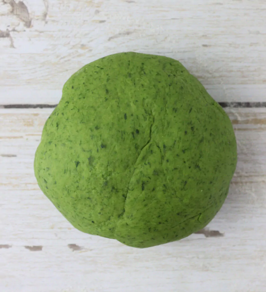 image showing how green pasta dough ball looks like when kneaded enough, before chilling it in the refrigerator