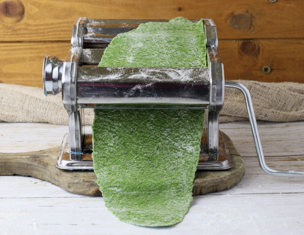 rolling a first sheet of green pasta dough on the first setting of the pasta maker machine 