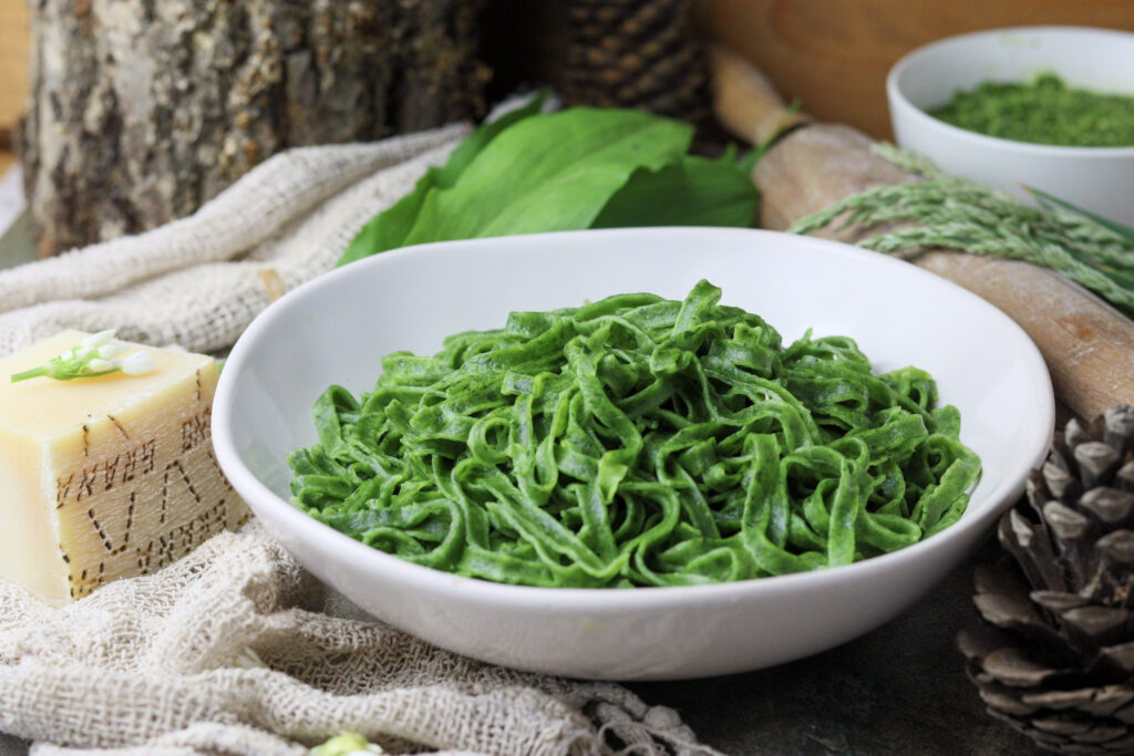 a plate of green pasta served with wild garlic pesto and grana padano cheese in the background 