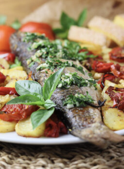 oven baked grey mullet served with potatoes, vegetables, garlic sauce and garnished with fresh basil leaf