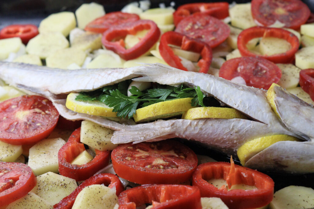 image showing how to season the belly cavity of the mullet fish with salt and adding lemon slices, garlic cloves and parsley for a better taste. Also stacking lemon slices in the gill openings. 