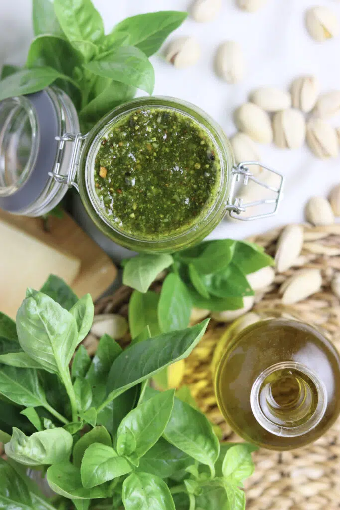 image of yummy basil pesto with pistachios and grana padano with basil, pistachios and a bottle of organic olive oil in the background