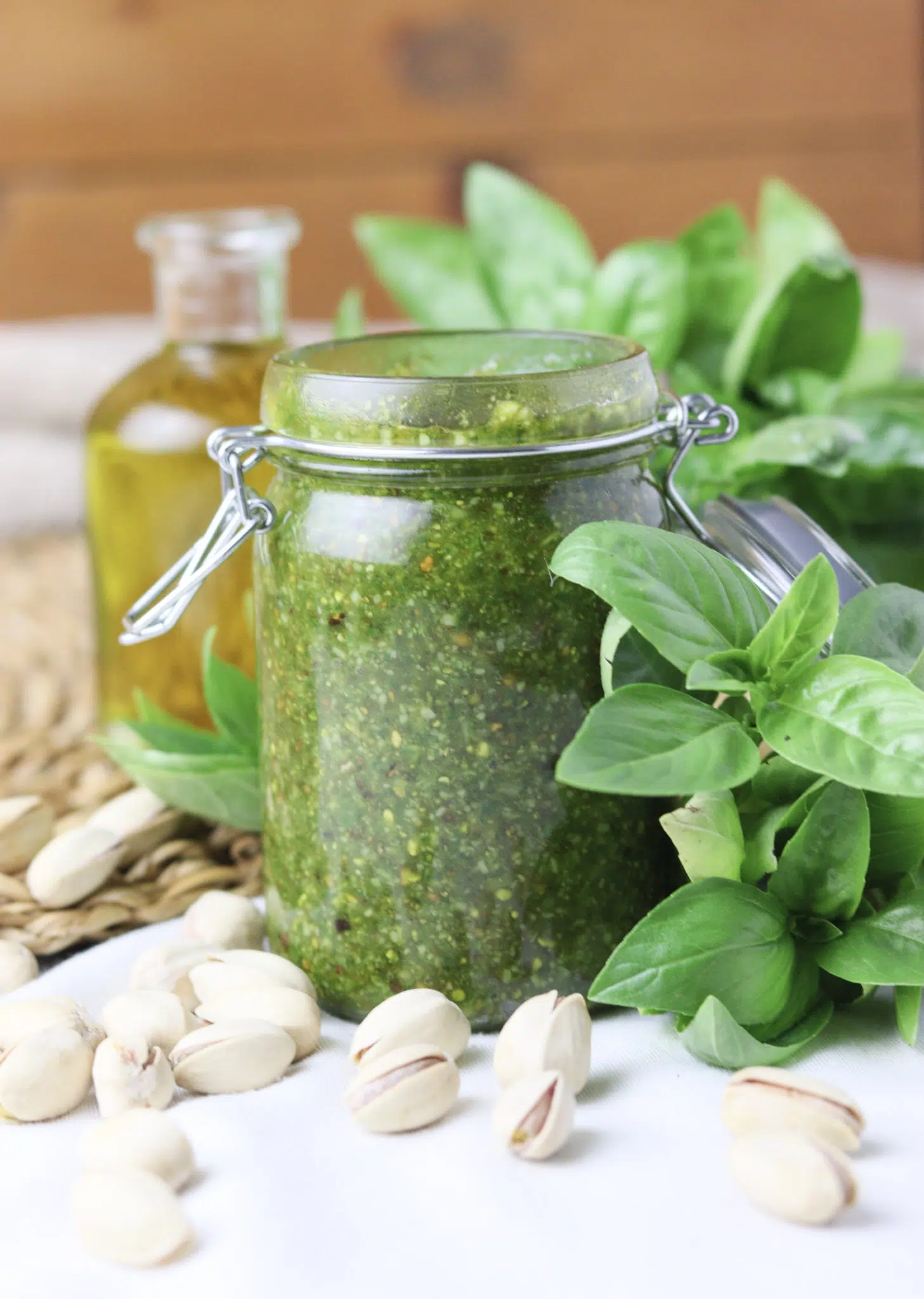 image of basil pesto with pistachios in a jar, with pistachios and olive oil in the background